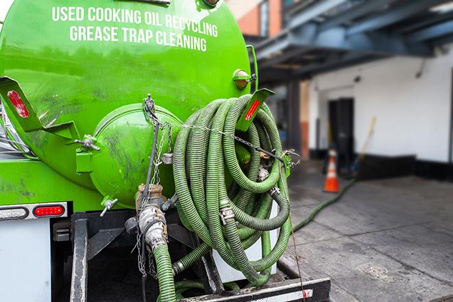 a professional plumber using a pump to empty a grease trap in Castroville